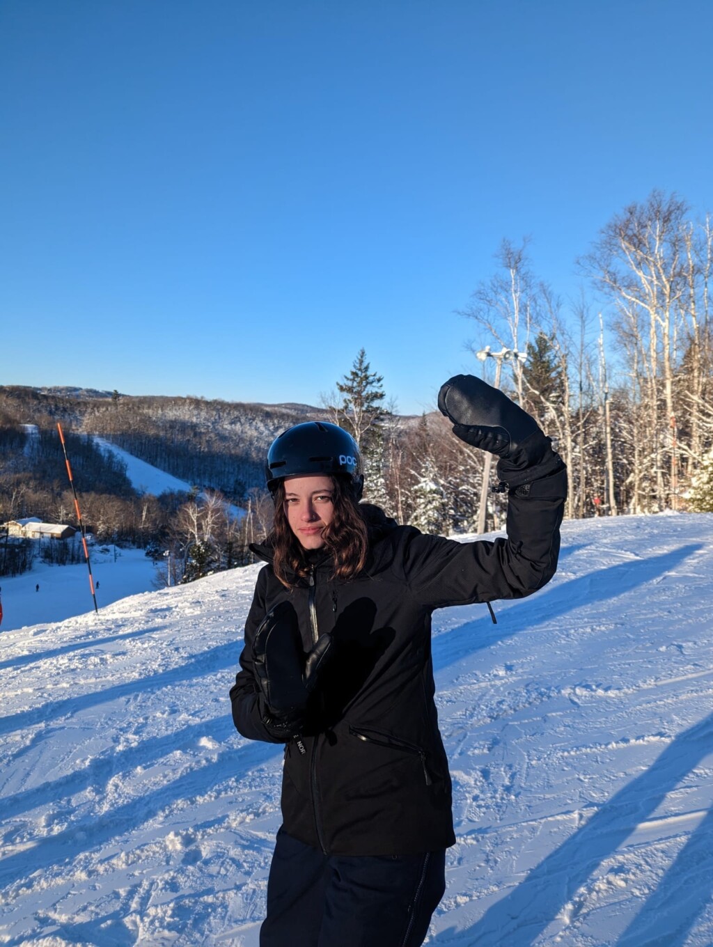 personne bilingue sur une piste de ski en habit noir complet et fait signe de salut avec la main