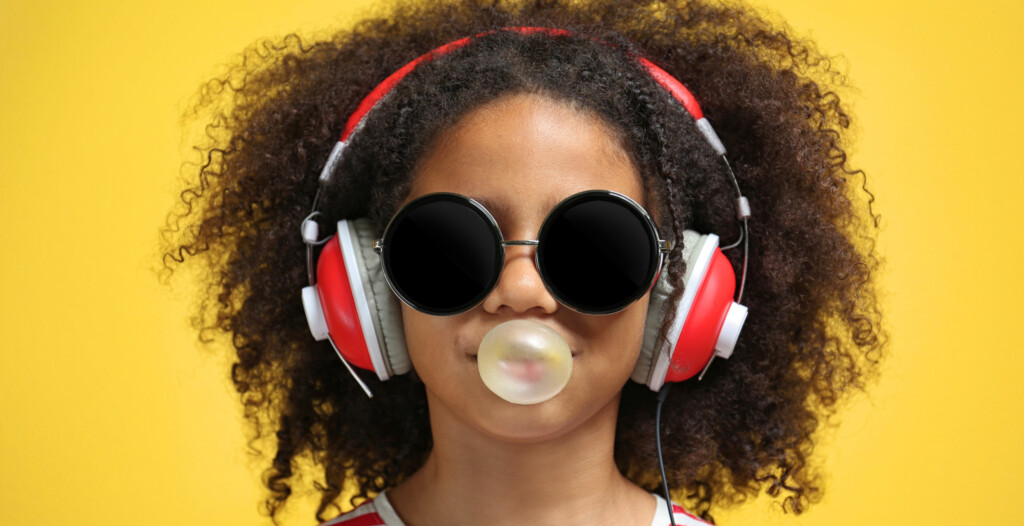 jeune fille avec lunettes ronde et écouteurs rouge sur arriere plan jaune avec gomme baloune pret à l'aventure
