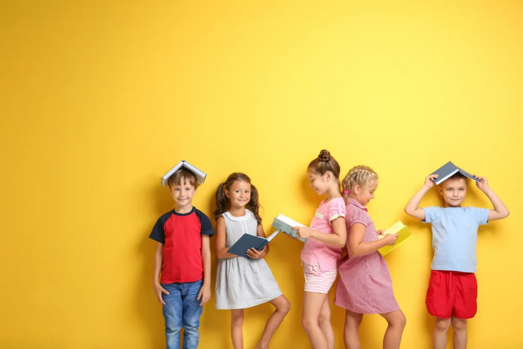 A group of five diverse children standing against a bright yellow wall, playfully interacting with books by reading them or balancing them on their heads, symbolizing the fun and discovery found in literacy. Story Un groupe de cinq enfants d'origines diverses debout contre un mur jaune vif, interagissant joyeusement avec des livres en les lisant ou en les posant sur leur tête, symbolisant le plaisir et la découverte par la lecture. contes